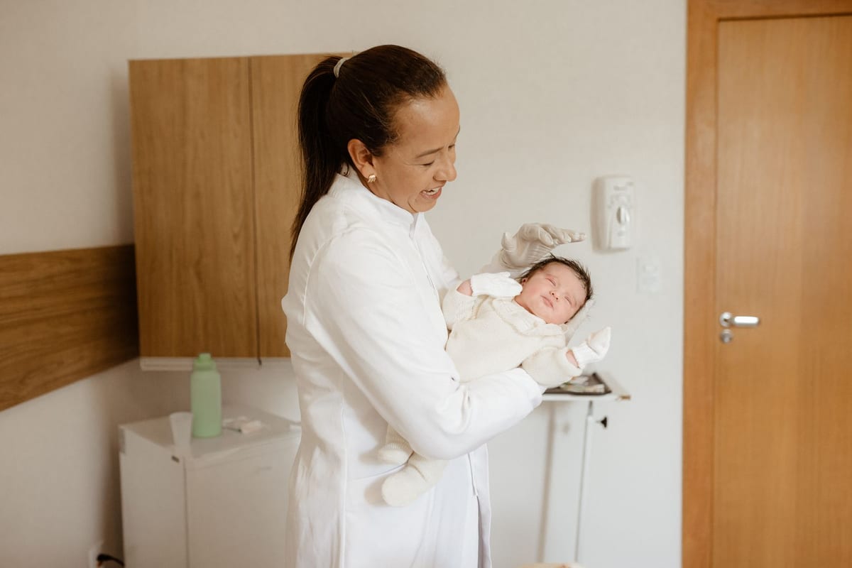 A clinician in a white coat holding a newborn in a clinic room